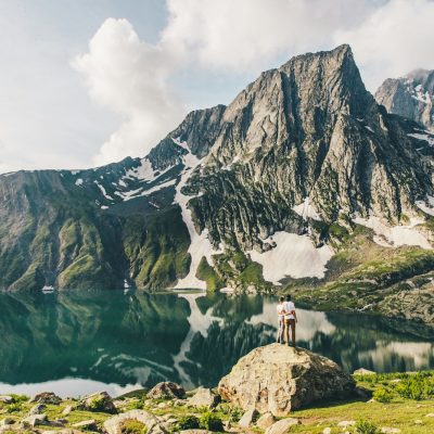 person standing on rock near lake and mountain range